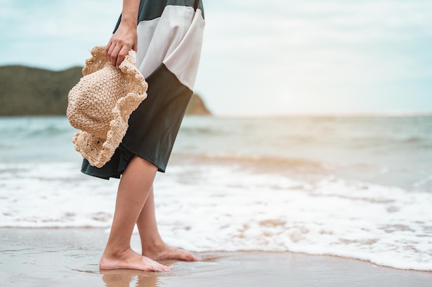 Szczęśliwe Azjatyckie Kobiety Z Trzymającym Kapelusz Stoją, Aby Otrzymać Wiatr I Cieszyć Się życiem Na Wakacjach Na Plaży. Plaża, Lato, Styl Windy, Pozytywny Nastrój, Podróże, Koncepcja Relaksu.