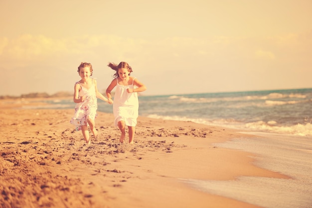szczęśliwe dwie małe dziewczynki bawią się i bawią na pięknej plaży, uciekając przed radością