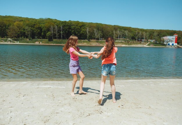 Szczęśliwe dwie małe dziewczynki bawią się i radośnie biegają po plaży skaczą po piasku