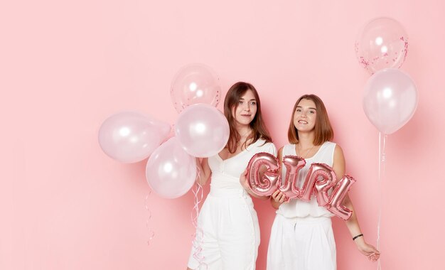Szczęśliwe dwie młode kobiety ubrane na biało trzyma balony na różowym tle