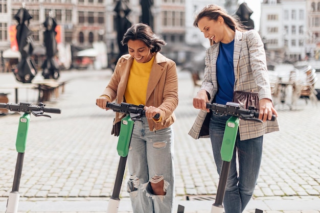 Szczęśliwe dwie modne koleżanki w centrum miasta za pomocą escootera