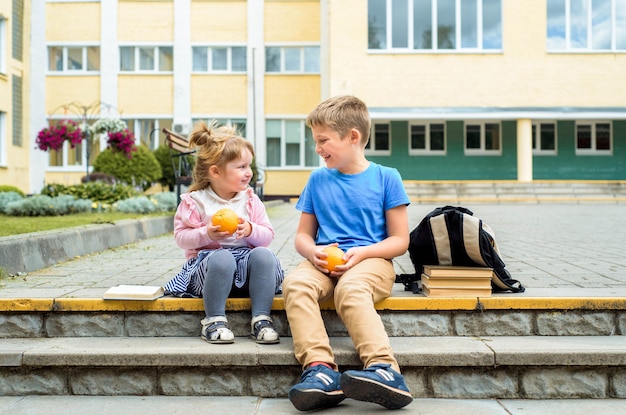 Szczęśliwe dzieci bawiące się na podwórku szkolnym w ciągu dnia. Śniadanie w szkole, owoce i soki. Stos podręczników, książek. szczęśliwa przyjazna siostra i brat