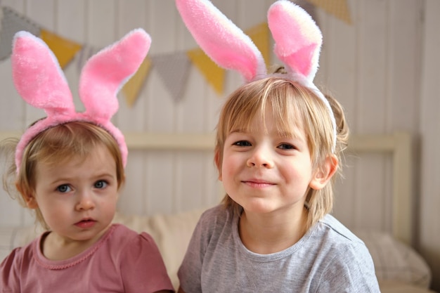 Szczęśliwe dzieci, dziewczynka i chłopiec w opasce z uszami królika, bawiące się w domu w sypialni z kolorowymi pisankami