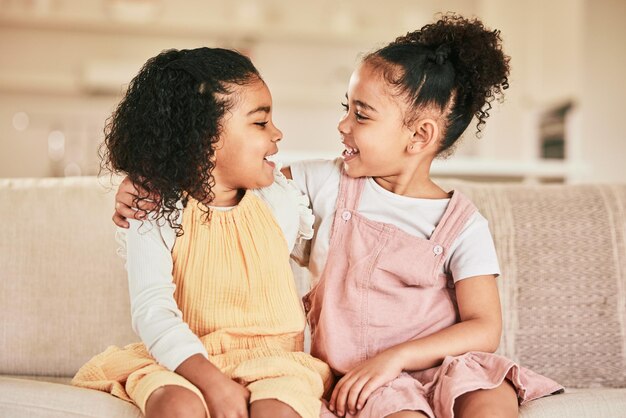 Zdjęcie szczęśliwe dzieci i siostry przytulające się na sofie podczas łączenia się w salonie ich domu przyjaźń szczęścia i dziewczynki obejmujące się podczas rozmowy i spędzania czasu razem w domu