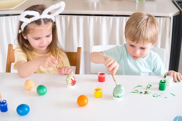 Zdjęcie szczęśliwe dzieci malują jaja wielkanocne w kuchni.
