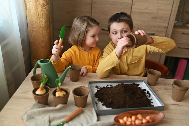 Zdjęcie szczęśliwe dzieci sadzą rośliny w domu dziewczynka i chłopiec sieją nasiona w naturalnych doniczkach ogrodniczych