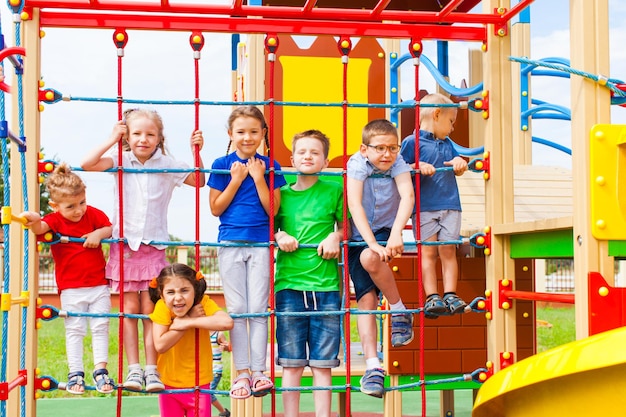 Szczęśliwe dzieci spędzają czas na wspinaniu się po siatce linowej podczas przerwy w przedszkolu lub szkole podstawowej. Plac zabaw szkolny z kolorową siatkową liną