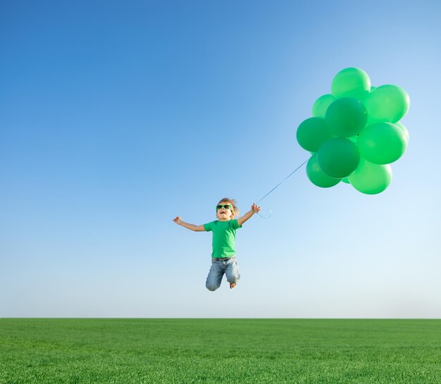 Szczęśliwe dziecko bawi się jasnymi wielokolorowymi balonami na świeżym powietrzu. Dziecko zabawy w zielonym polu wiosny na tle błękitnego nieba. Koncepcja zdrowego i aktywnego stylu życia