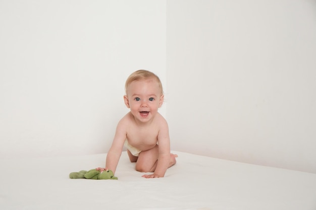 Szczęśliwe dziecko bawi się zieloną pluszową zabawką na białym łóżku w białym pokoju