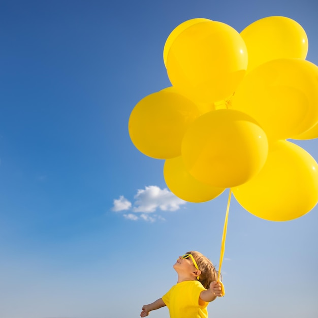 Szczęśliwe dziecko bawi się żółtymi balonami na świeżym powietrzu. Dziecko zabawy na tle błękitnego nieba latem. Koncepcja wolności i aktywnego stylu życia