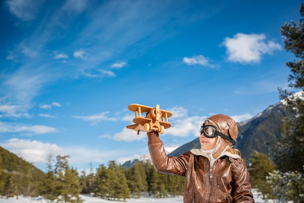 szczęśliwe dziecko bawiące się samolocikiem na tle zimowego nieba dzieciak pilot bawiący się na świeżym powietrzu