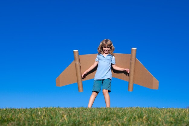 Szczęśliwe dziecko bawiące się zabawkami skrzydłami na tle letniego nieba Lider sukcesu dzieci i koncepcja zwycięzcy
