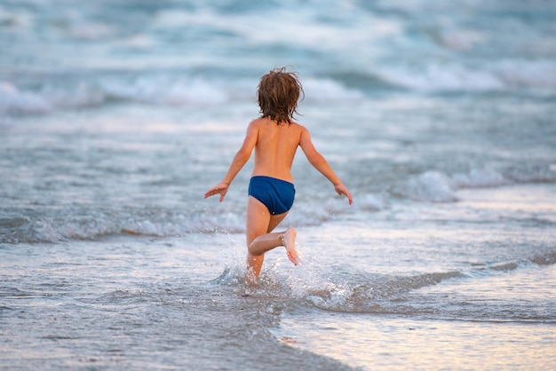 Szczęśliwe dziecko biegające w morzu dziecko chłopiec bawi się na wakacjach na plaży i zdrowe dzieci