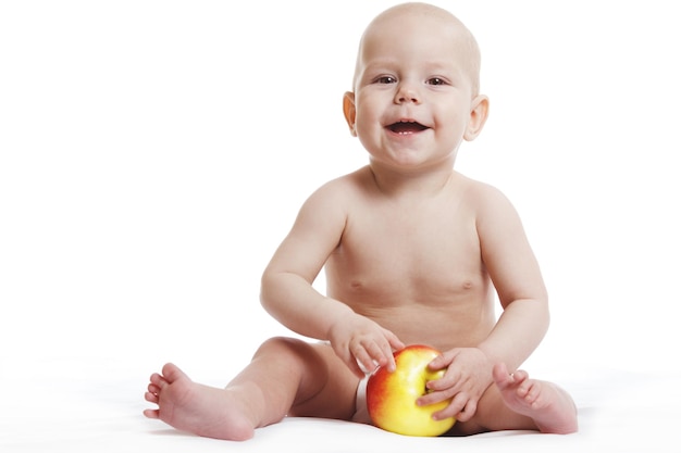 Szczęśliwe dziecko chłopiec siedzi w pieluszce i je czerwone żółte jabłko niebieskie oczy patrząc w róg na białym tle
