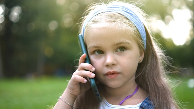 Szczęśliwe dziecko dziewczynka o rozmowie rozmawiając na jej sellphone w parku latem.