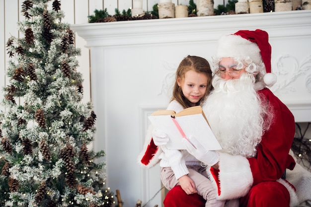 Szczęśliwe dziecko dziewczynka przytulanie Świętego Mikołaja podczas czytania książki
