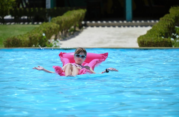 Szczęśliwe dziecko dziewczynka relaksuje się na dmuchanym materacu w basenie w słoneczny letni dzień podczas tropikalnych wakacji Koncepcja aktywności letnich