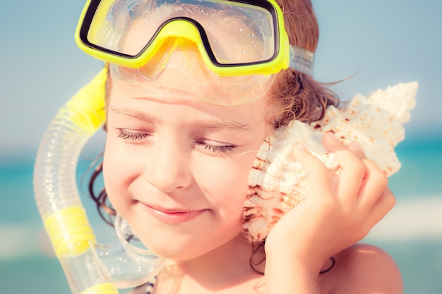 Szczęśliwe dziecko grając na plaży Dziecko słucha muszli Koncepcja wakacji letnich