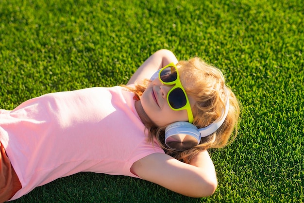 Szczęśliwe dziecko lubi słuchać muzyki w słuchawkach na tle zielonej trawy Zabawny dzieciak w słuchawkach