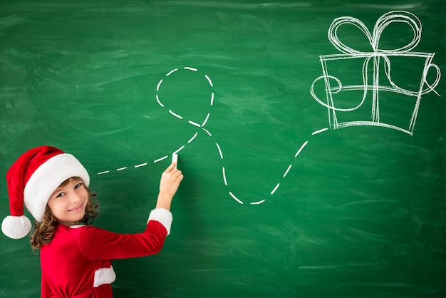 Szczęśliwe dziecko noszące Świętego Mikołaja rysuje na zielonej tablicy