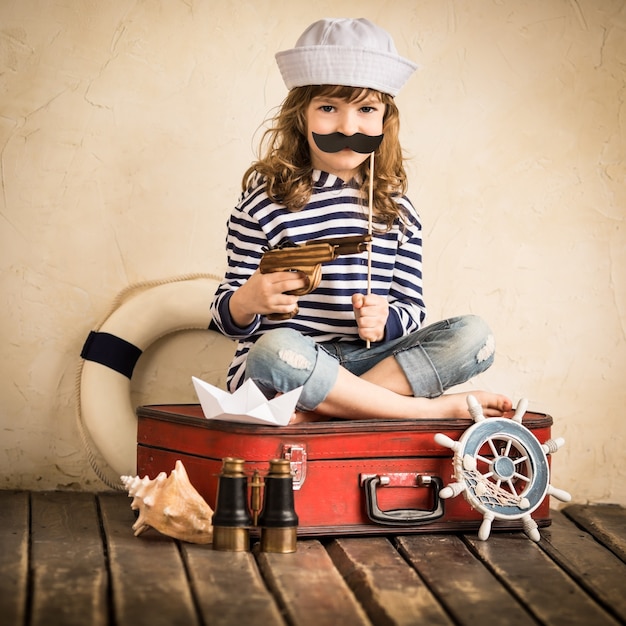 Szczęśliwe dziecko pirat bawi się zabawkami łodzi żaglowej w pomieszczeniu. Koncepcja podróży i przygody