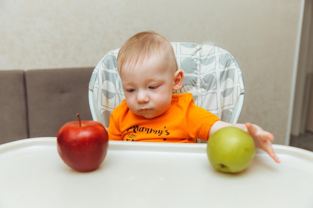 Szczęśliwe dziecko siedzi w wysokim krzesełku i je jabłka