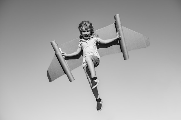 Szczęśliwe dziecko skaczące i bawiące się zabawkowymi skrzydłami na tle letniego nieba Lider sukcesu dzieci i