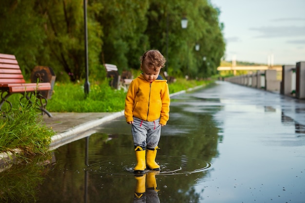 Szczęśliwe dziecko stać w kałuży Dziecko bawi się w błocie z pluskiem w parku jesień. Zabawa na świeżym powietrzu w czasie deszczu