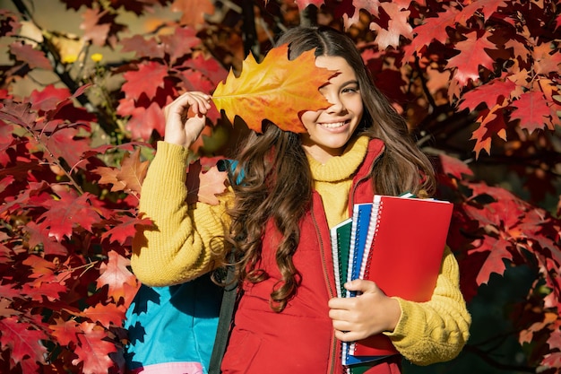 Szczęśliwe dziecko trzyma notatnik na tle jesiennych liści