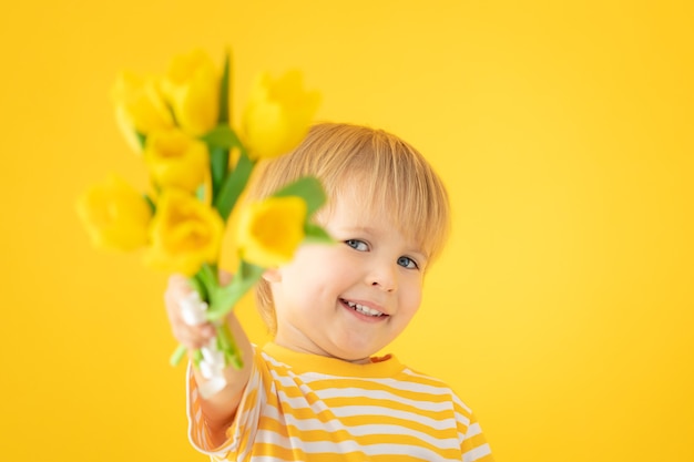 Szczęśliwe Dziecko Trzymając Wiosenny Bukiet Tulipanów Na żółtej ścianie.