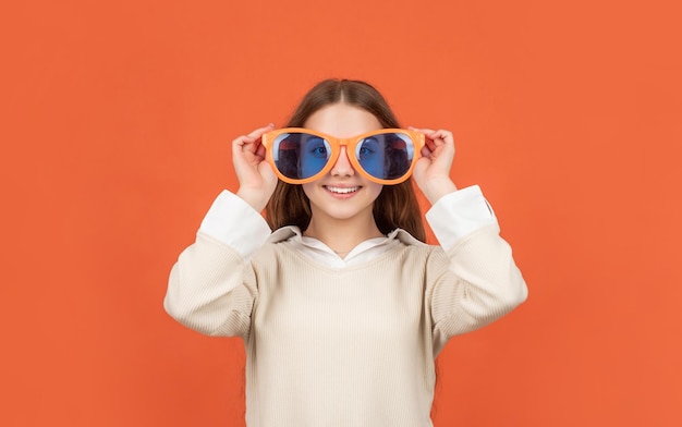 Szczęśliwe dziecko w imprezowych okularach na pomarańczowym tle zabawy
