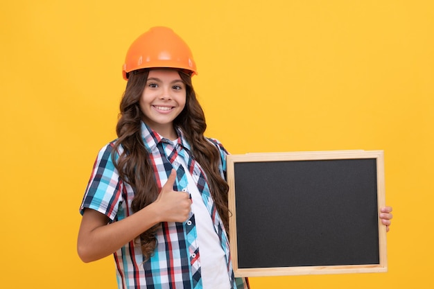 Szczęśliwe dziecko w kasku przedstawiające szkolną tablicę z reklamą pokazuje kciuk w górę kopiuje przestrzeń edukacja szkolna