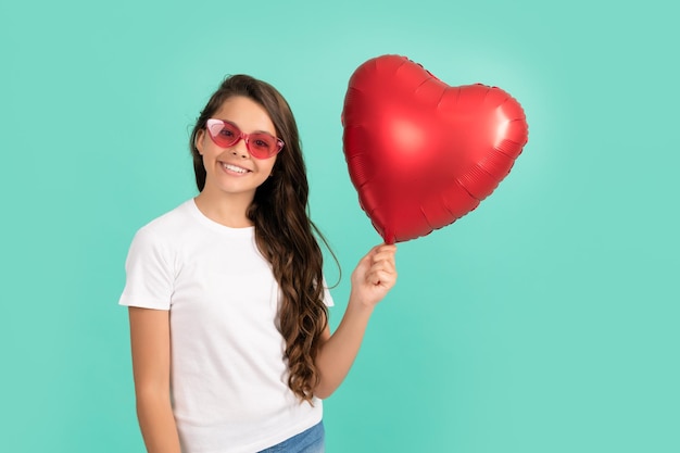 Szczęśliwe dziecko w okularach przeciwsłonecznych trzyma balon z czerwonym sercem na walentynki symbol miłości kochanie