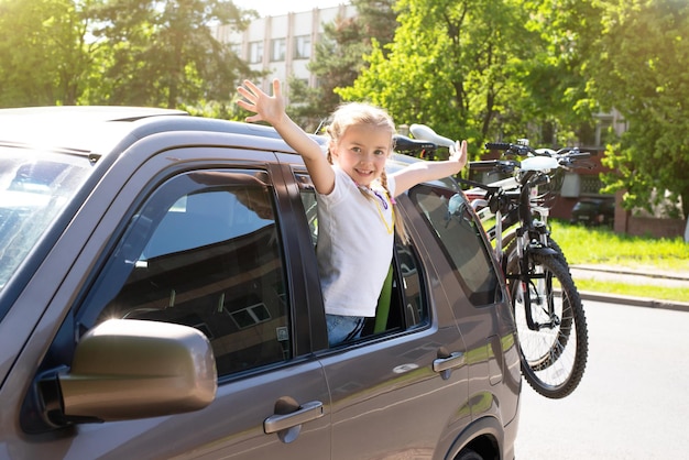 Szczęśliwe dziecko wygląda przez okno samochodu podczas podróży rowery w bagażniku samochodu