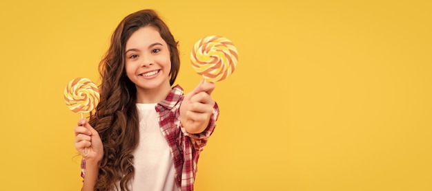 Szczęśliwe dziecko z długimi kręconymi włosami pokazuje cukierki karmelowe Lollipop na żółtym tle opieka dentystyczna Nastolatek dziecko ze słodyczami plakat banner nagłówek kopia przestrzeń
