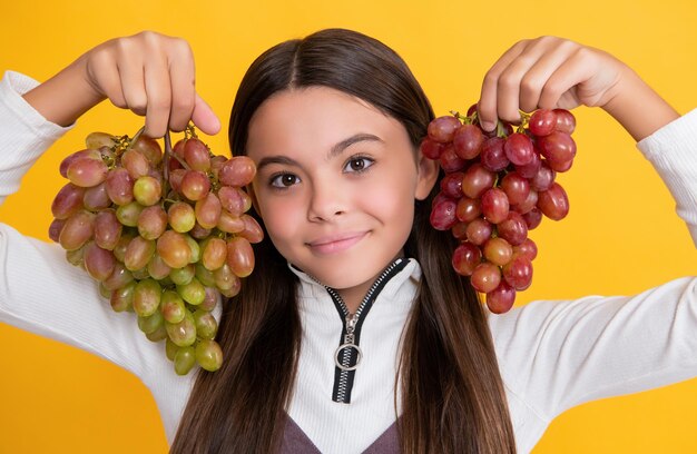 Szczęśliwe dziecko z kiścią świeżych winogron na żółtym tle