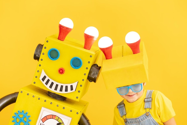 Szczęśliwe dziecko z robotem na żółtym tle. Zabawne dziecko bawiące się w domu. Sukces, kreatywna i innowacyjna koncepcja technologii