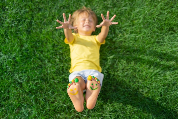 Zdjęcie szczęśliwe dziecko z uśmiechem na stopach na świeżym powietrzu dziecko leżące na zielonej wiosennej trawie koncepcja ekologii i zdrowego stylu życia widok z góry