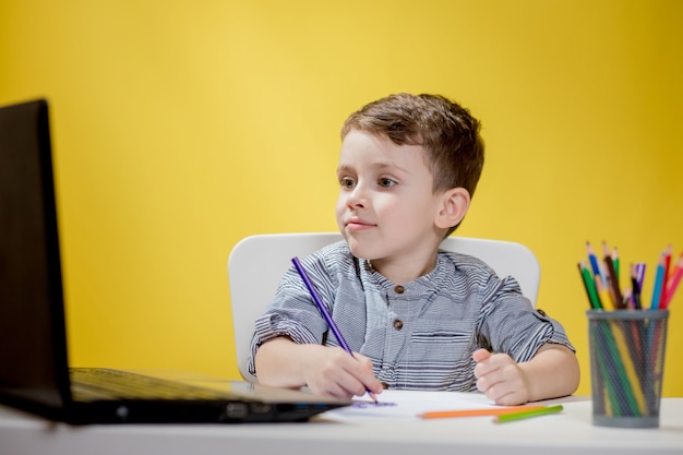 Szczęśliwe dziecko za pomocą cyfrowego laptopa odrabiania lekcji na żółto. Dystans społeczny, edukacja online na odległość.