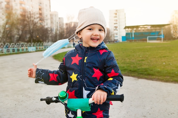 Szczęśliwe dziecko zdejmuje maskę z twarzy na ulicy i radośnie oddycha świeżym powietrzem. Relaks kwarantanny, możliwość spaceru po ulicy. Jazda rowerem.