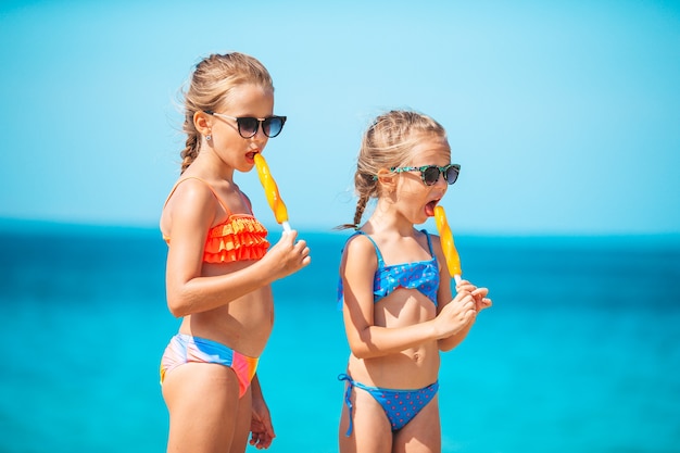 Szczęśliwe dziewczynki jedzenie lodów podczas wakacji na plaży ludzie dzieci, przyjaciele i koncepcja przyjaźni