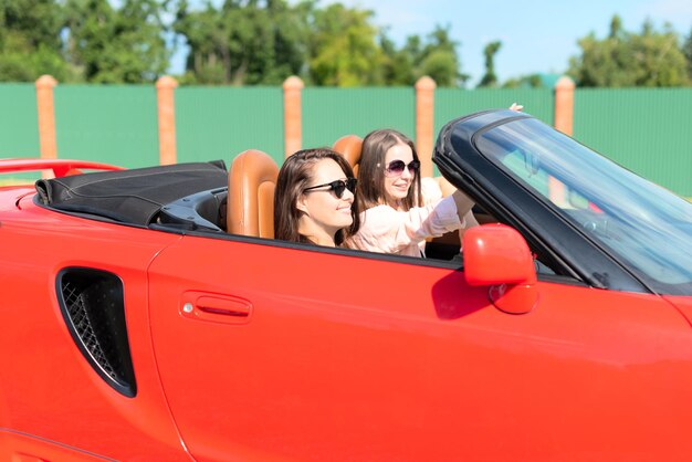 Szczęśliwe dziewczyny jadące czerwonym kabrioletem podczas podróży, bawiące się razem