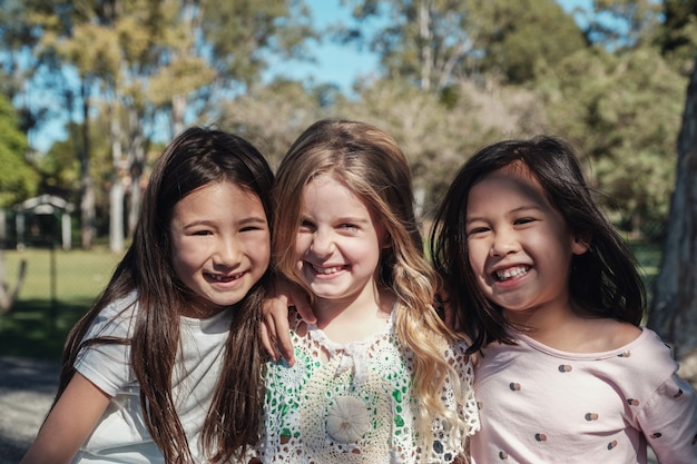 Szczęśliwe i zdrowe mieszane młode dziewczynki etniczne przytulające się i uśmiechnięte w parku, najlepsi przyjaciele i przyjaźń