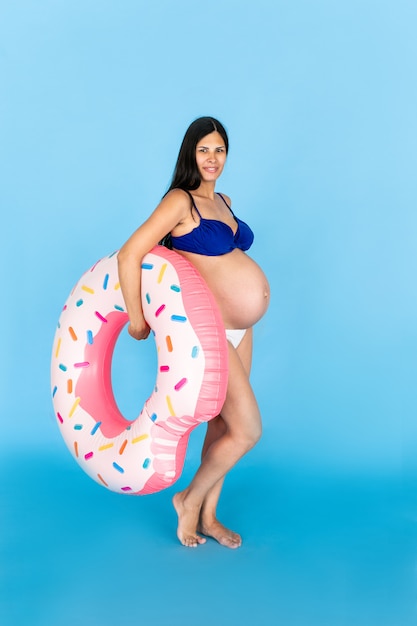 Szczęśliwe kobiety w ciąży w strój kąpielowy z pierścieniem pływanie pierścień na kolorowej ścianie niebieski