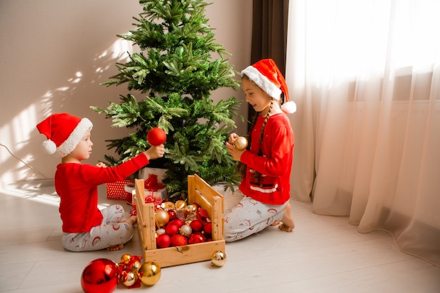szczęśliwe małe dzieci w czerwonej piżamie ozdabiają choinkę w salonie zimowej koncepcji