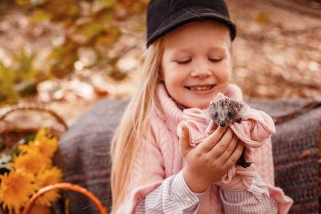 Szczęśliwe małe dziecko dziewczynka z uroczym jeżem Portret dziecka ze zwierzakiem w jesiennej naturze z dyniami i słomką trzymającą kubek gorącego napoju
