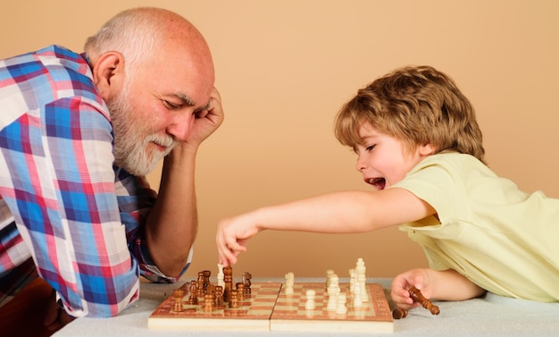 Szczęśliwe małe dziecko gra w szachy z dziadkiem. Relacja rodzinna z dziadkiem i wnukiem. Dziadek i wnuk grając w grę planszową.