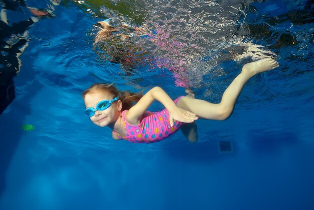 Szczęśliwe małe dziecko pływa pod wodą w basenie, patrząc w kamerę i uśmiechając się