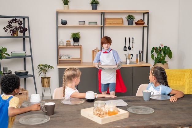 Szczęśliwe młode dzieci z surowymi ciasteczkami na tacy stojącej przy stole w kuchni