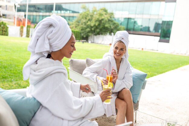 Szczęśliwe młode piękne kobiety cieszące się zabawą po zabiegach spa razem w luksusowym hotelu, noszące ręczniki na głowach i szlafroki.